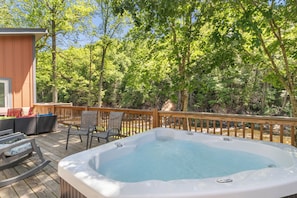 A hot tub on a wooden deck with chairs and a table, surrounded by trees. - Hot Tub+Fire Pit, On the River, WiFi, Grill, Cozy! (Burnsville)