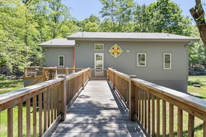 A wooden deck leading to a building with a grey exterior and a decorative peace symbol on the wall. - Hot Tub+Fire Pit, On the River, WiFi, Grill, Cozy! (Burnsville)