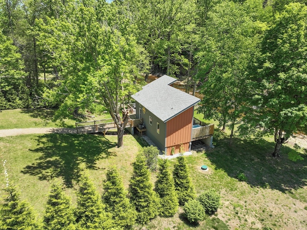 A small cabin with a wooden deck, surrounded by dense trees and a clear sky.