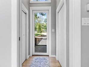 A narrow hallway with a wooden floor leading to a door with a glass panel.