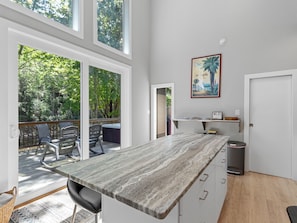 A modern kitchen with a marble countertop, a hot tub, and a view of a forested area. - Hot Tub+Fire Pit, On the River, WiFi, Grill, Cozy! (Burnsville)