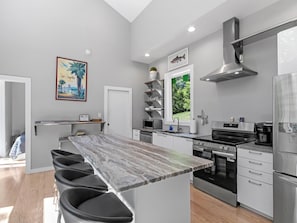 A modern kitchen with a central island, stainless steel appliances, and a view of greenery outside.