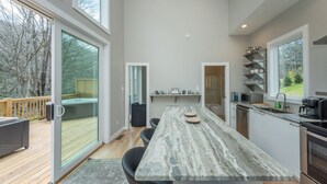Eine moderne Küche mit Marmorarbeitsplatte, eingebauten Geräten und großen Fenstern mit Blick auf eine Terrasse und Bäume.