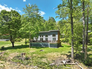 A two-story house with a deck, surrounded by trees and grass. - Hot Tub+Fire Pit, On the River, WiFi, Grill, Cozy! (Burnsville)
