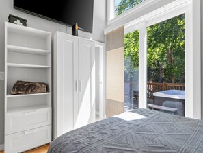 A bedroom with a large bed, a wardrobe, a television, and a view of an outdoor hot tub area. - Hot Tub+Fire Pit, On the River, WiFi, Grill, Cozy! (Burnsville)