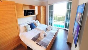 A modern bedroom with a large bed, wooden paneling, a TV, and a balcony with a view.