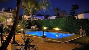 A swimming pool surrounded by palm trees and a hedge, with a clear night sky.