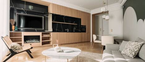 A modern living room with a sofa, a coffee table, a TV, and a kitchen area.