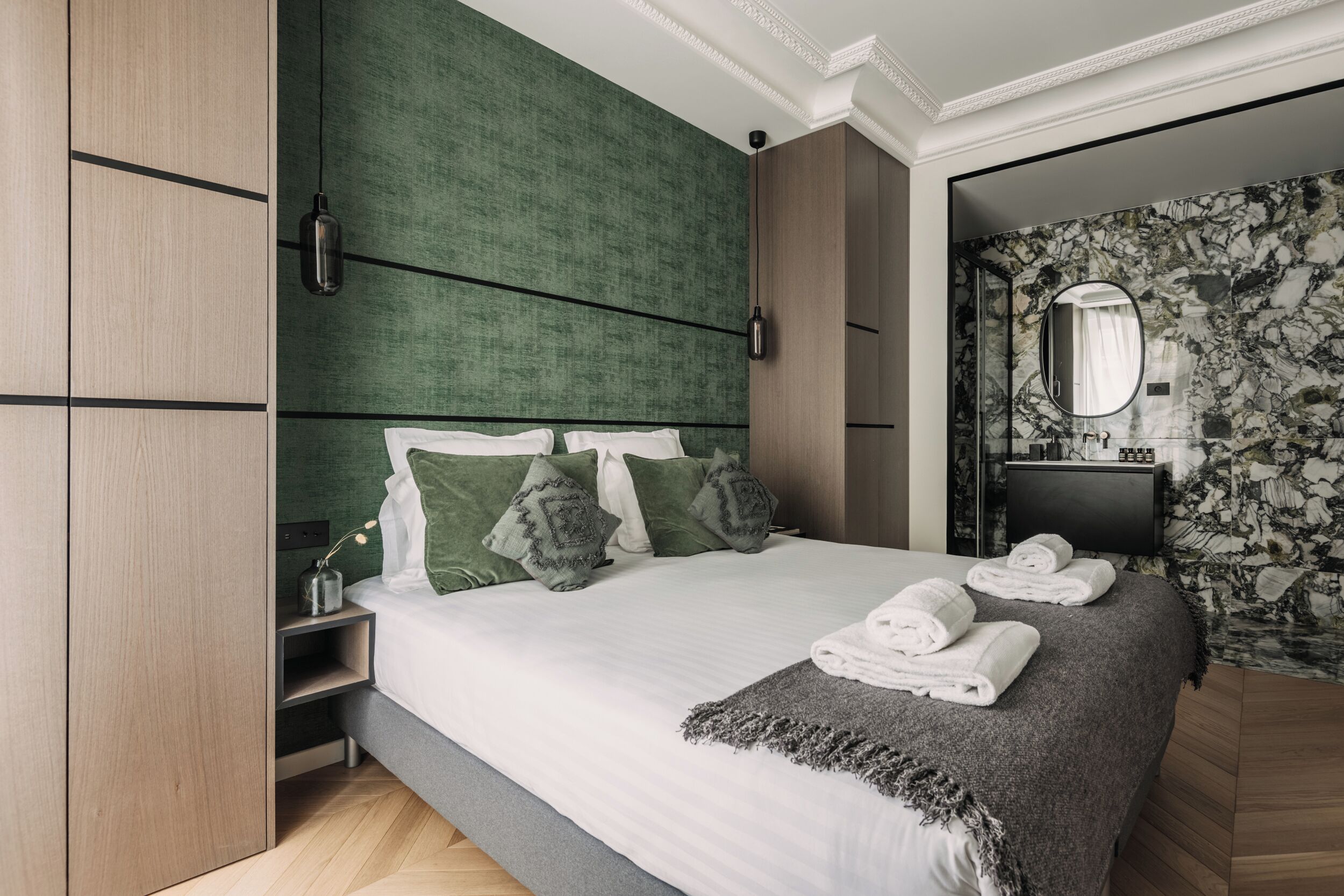 Ein modernes Schlafzimmer mit einem großen Bett, einem grünen Kopfteil und einer Wand mit Marmoroptik.