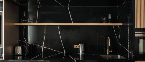 A modern kitchen with black marble countertops, wooden cabinets, and a stainless steel sink.