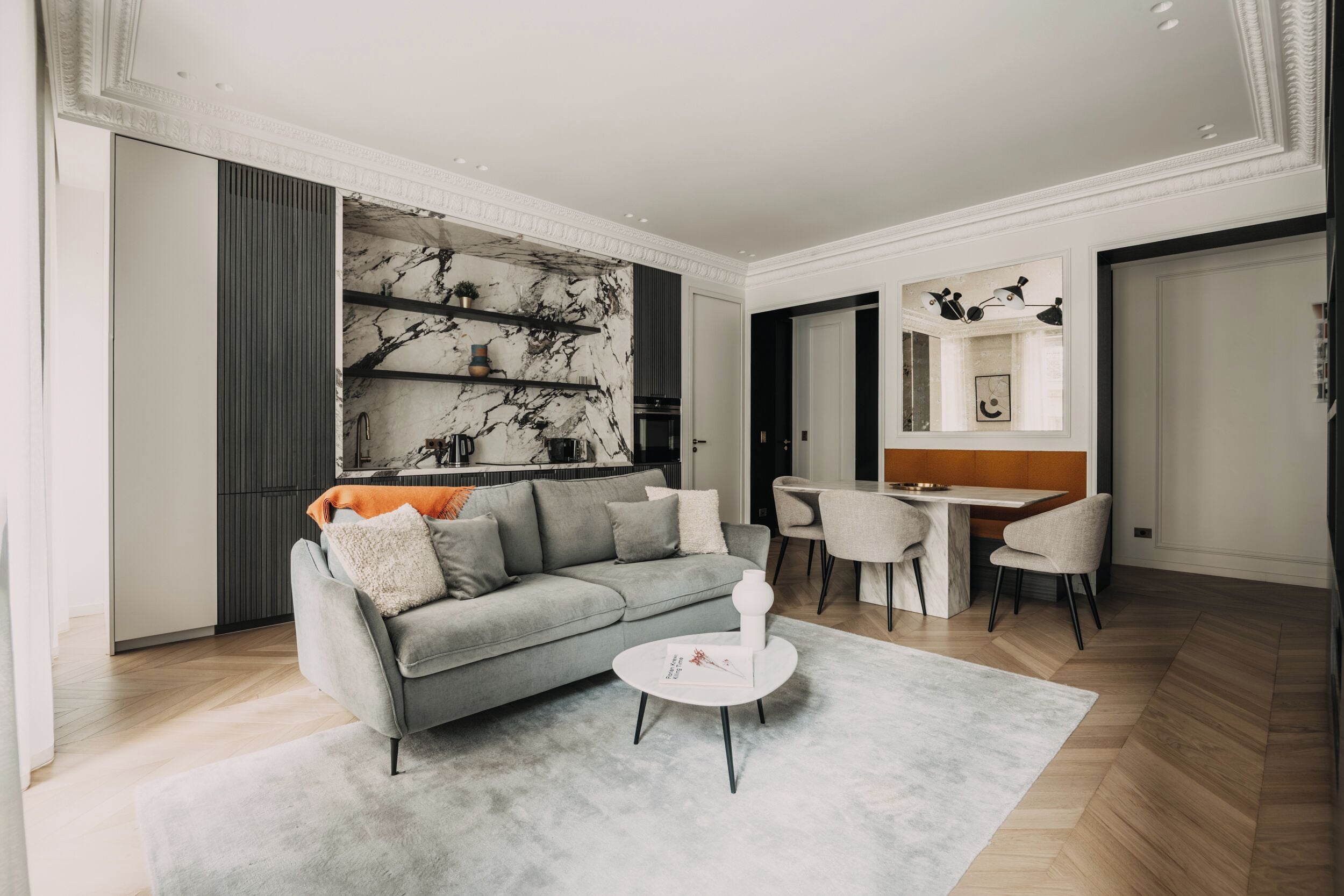 Un salon moderne avec un canapé gris, une table basse ronde et un mur décoratif en marbre.