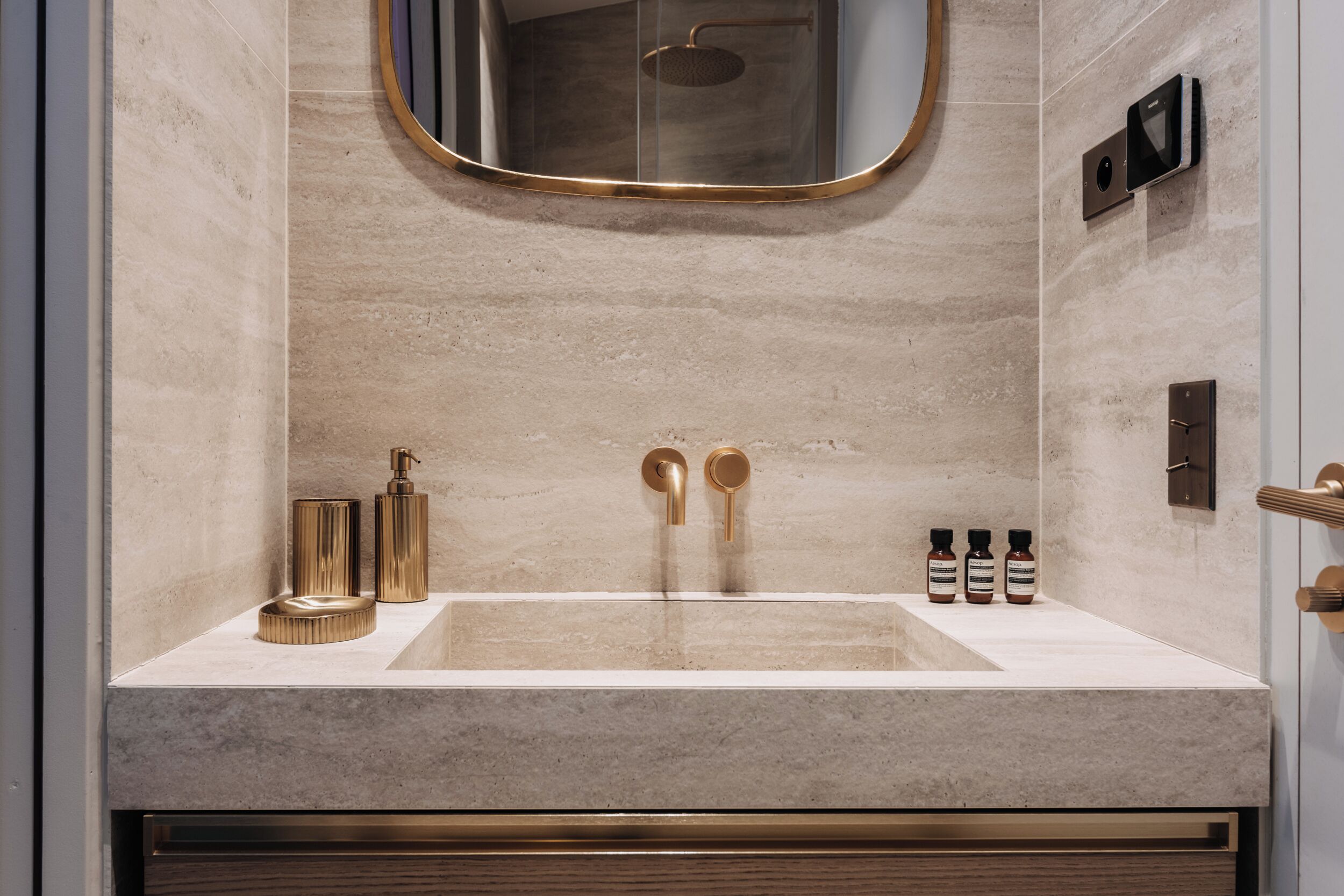 A modern bathroom with a large sink, gold fixtures, and a mirror above the sink.