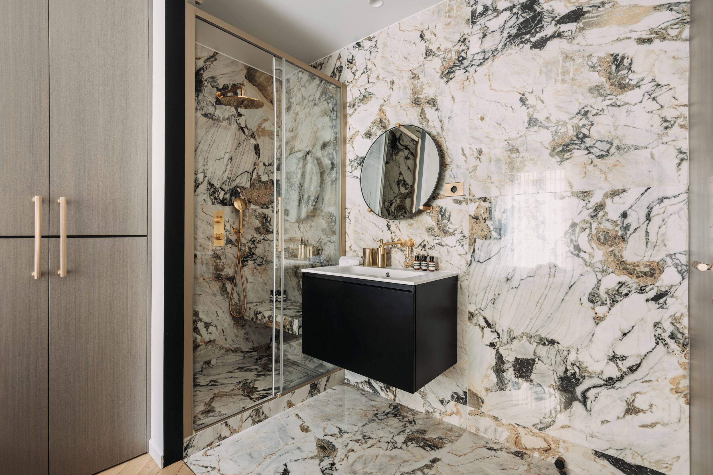 A bathroom with a marble wall, a black vanity, and a glass shower enclosure.
