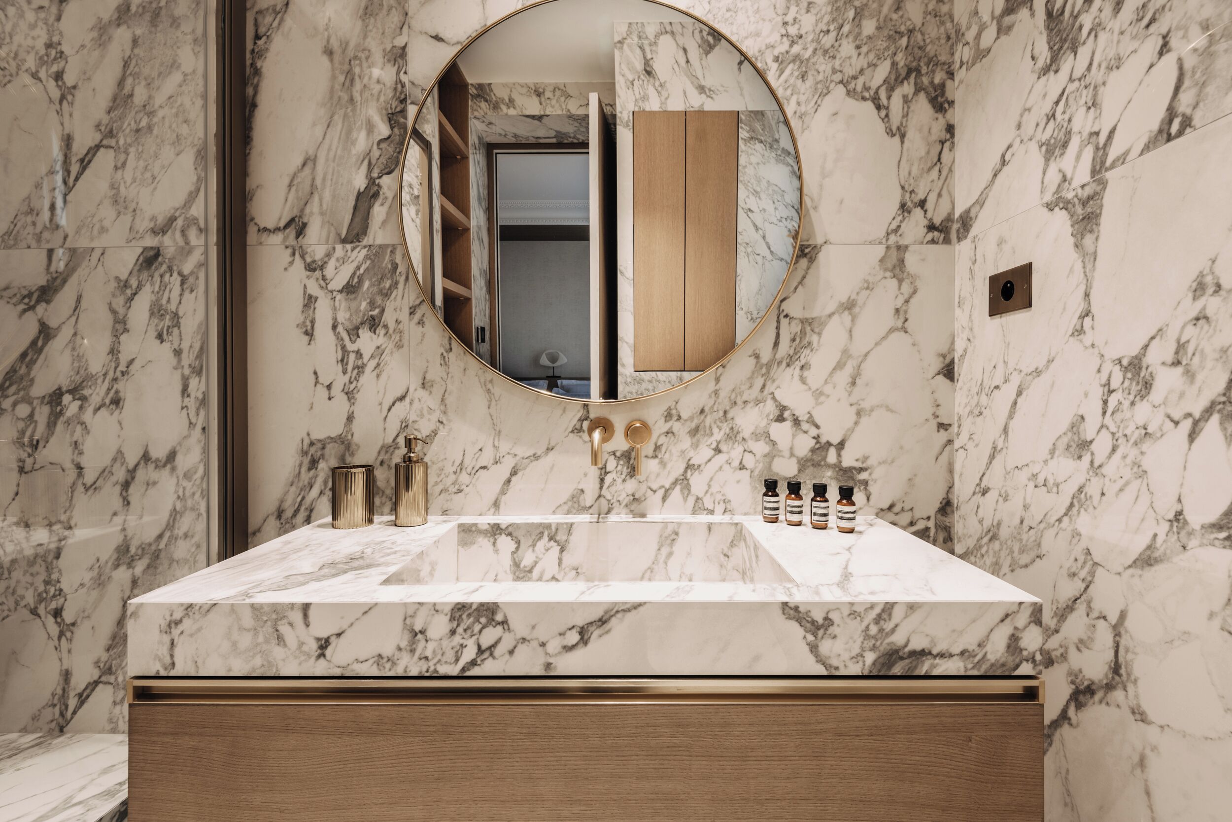 A bathroom with a marble sink, a round mirror, and a wooden vanity.