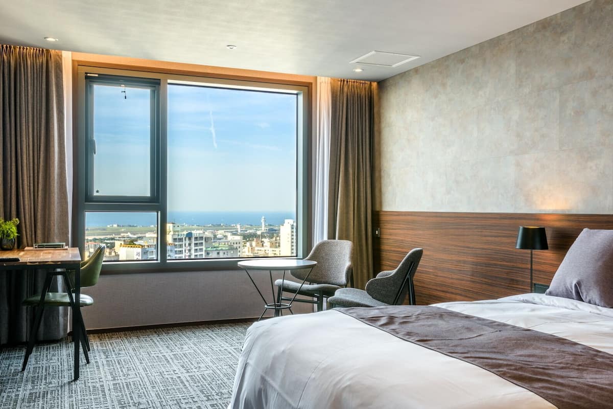Hotellihuone, jossa on suuri ikkuna, sänky, työpöytä ja tuoli.