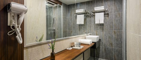 A modern bathroom with a wooden vanity, a glass shower enclosure, and a hairdryer mounted on the wall.