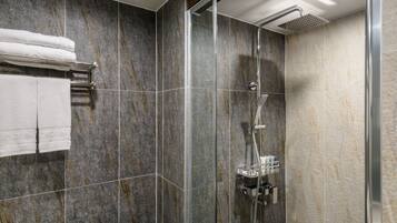Un baño moderno con ducha de vidrio, baldosas de mármol y un perchero con toallas dobladas.