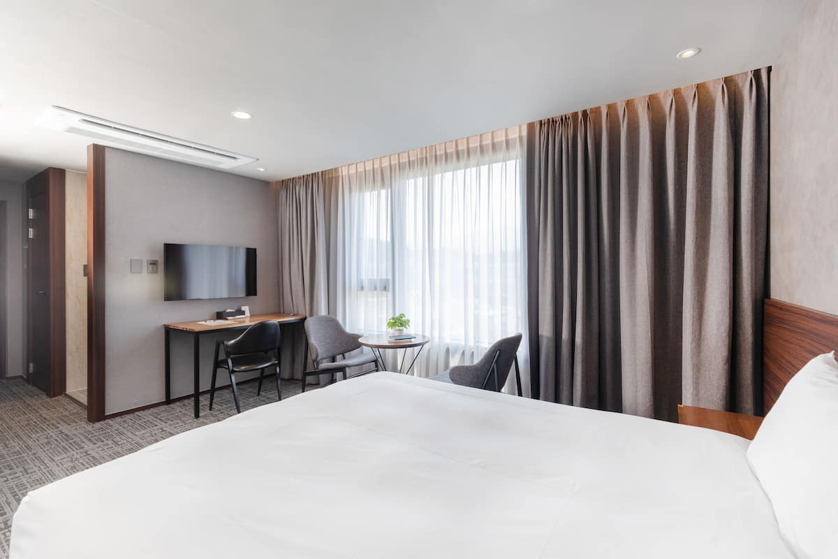 Hotellihuone, jossa on suuri sänky, työpöytä kahdella tuolilla, pieni pöytä, jossa on kasvi, ja seinälle asennettu televisio.