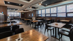 Un restaurant moderne avec un intérieur caractérisé par de hauts plafonds, des conduits apparents et de grandes fenêtres offrant une vue sur la ville.