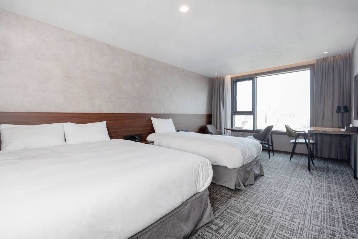 Hotellihuone, jossa on kaksi sänkyä, työpöytä ja tuoli.