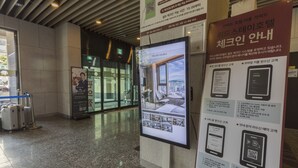 Un hall d’entrée moderne doté d’un kiosque d’information numérique, d’une porte d’entrée en verre et de bagages déposés près de l’entrée.