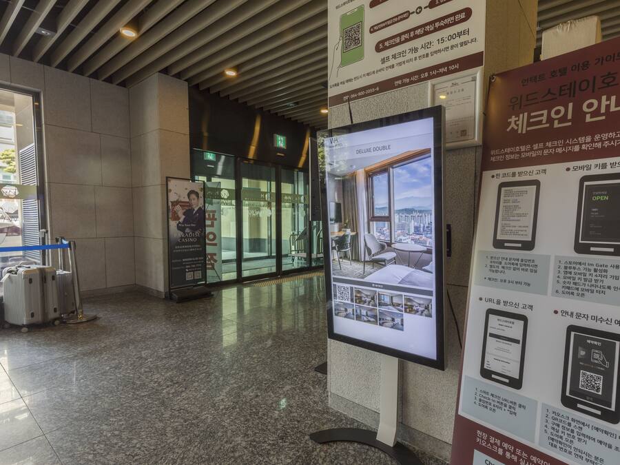 Una hall moderna con una postazione informativa digitale, un ingresso con porta in vetro e bagagli nei pressi dell'ingresso.