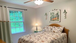 A bedroom with a bed, a window with curtains, a nightstand with a lamp, and wall art. - Serenity and Seclusion in Roan Mountain, TN  (Roan Mountain)