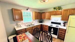 A kitchen with wooden cabinets, a microwave, a stove, a sink, and a dining table with chairs. - Serenity and Seclusion in Roan Mountain, TN  (Roan Mountain)
