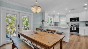 A modern kitchen with white cabinets, a wooden dining table, and a hanging chandelier.