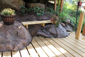 Eine Holzterrasse mit einer Bank, großen Steinen und Pflanzkübeln.