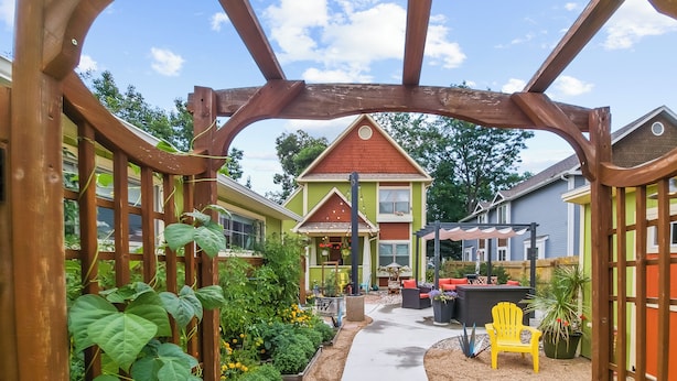 Un jardín con un porche de madera, un sendero y una zona de estar con mobiliario exterior.
