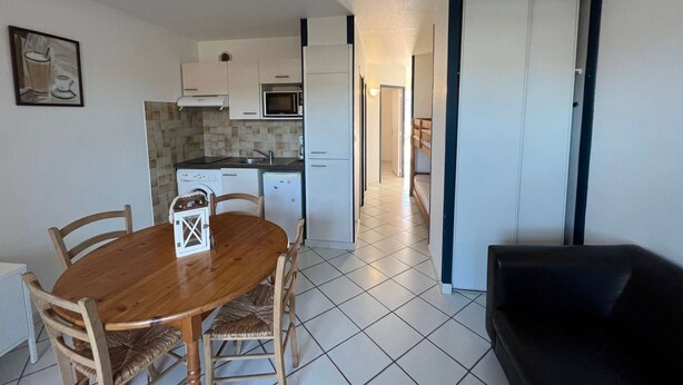 A compact living space with a kitchenette, a dining area with a wooden table and chairs, and a black sofa. - Flots Bleus N°1 Ground floor apartment of 35m² for 4 people (BISCARROSSE)