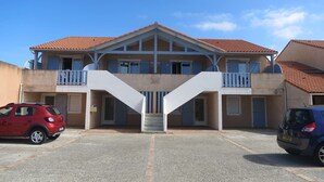 A two-story building with a central staircase and balconies. There are two cars parked in front. - Flots Bleus N°1 Ground floor apartment of 35m² for 4 people (BISCARROSSE)