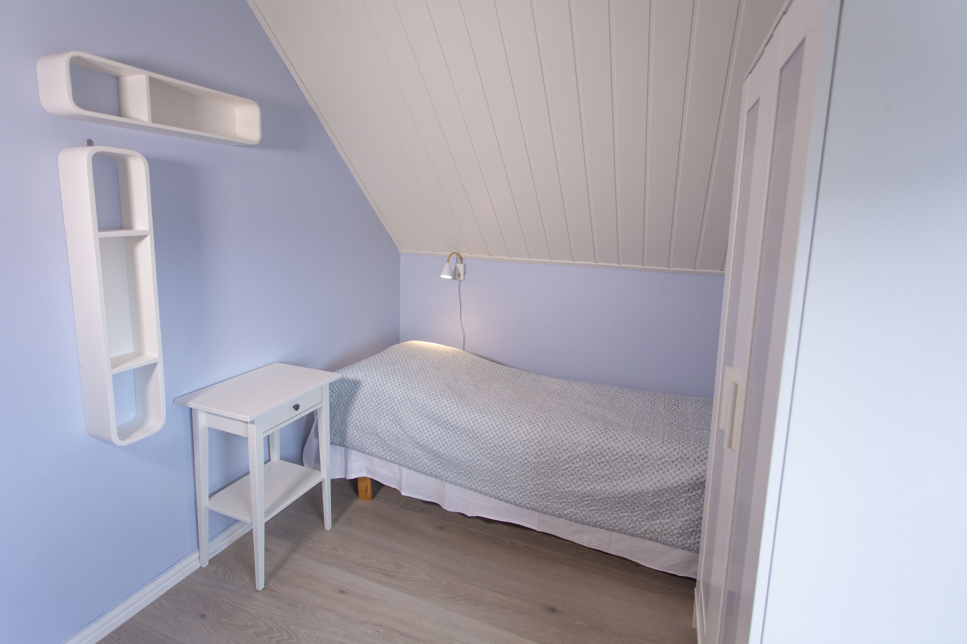 A small, neatly organized bedroom with a single bed, a nightstand, and a wall-mounted shelf.
