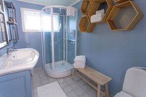 Een badkamer met een douchecabine van glas, een wastafel, een bankje en houten handdoekrekken.