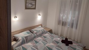 Una camera da letto con un letto, un ventilatore a soffitto, un comodino, una lampada a parete e una finestra con tende leggere.