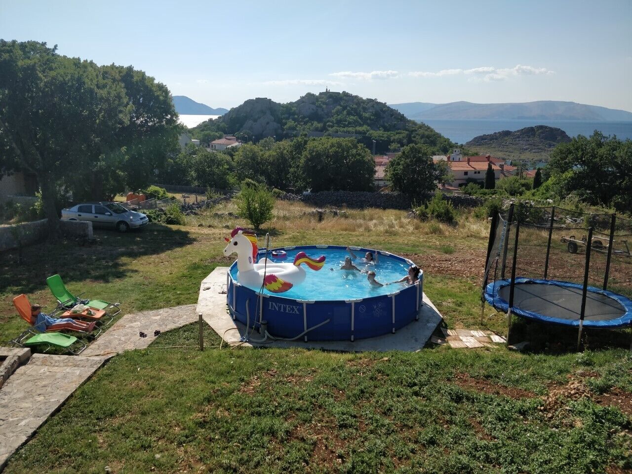 Un patio trasero con piscina, un trampolín y sillas de descanso.