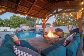An outdoor pool area with a fire pit, lounge chairs, and a covered seating area. - Family Retreat | Pool, Fire Pit, Ping Pong, Games (Pinellas Park)
