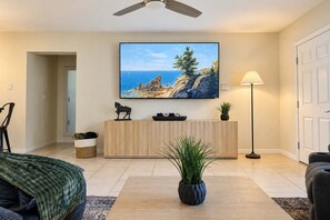 Una sala de estar moderna con un mostrador de recepción de madera, un cuadro colgado de una escena costera, una lámpara de pie y una planta en maceta.