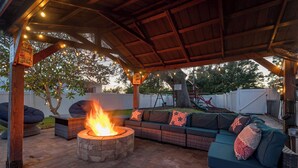 Un espacio al aire libre cubierto con una chimenea, asientos acolchados e iluminación con guirnaldas.