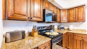 Una cocina con armarios de madera, un microondas de acero inoxidable, un tostador y una estufa.