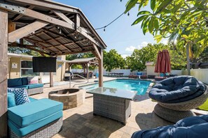 A covered outdoor area with a pool, seating, and a fire pit.