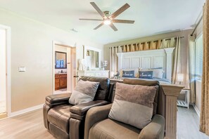 Un salón con un sillón reclinable de cuero, un ventilador de techo y vista hacia la cocina.