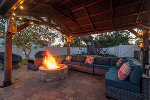 Un espacio al aire libre cubierto con una chimenea, asientos acolchados e iluminación con guirnaldas.