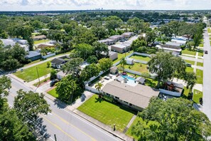 An aerial view of a residential area with houses, a swimming pool, and a clear road. - Family Retreat | Pool, Fire Pit, Ping Pong, Games (Pinellas Park)