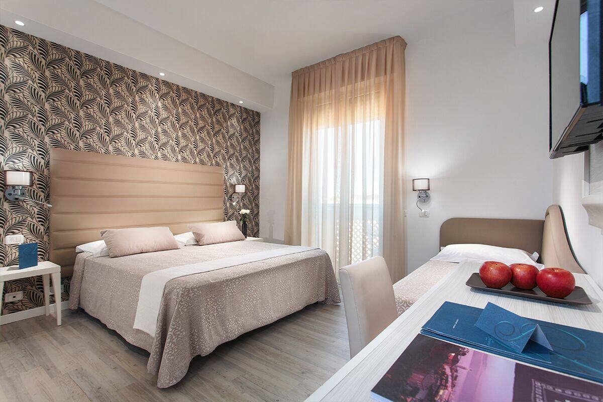 Quarto de hotel com uma cama grande, uma escrivaninha com cadeira, televisão e janela com cortinas.