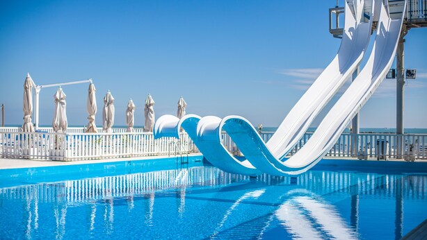 Una piscina con varias toboganes, sombrillas blancas y una valla blanca.