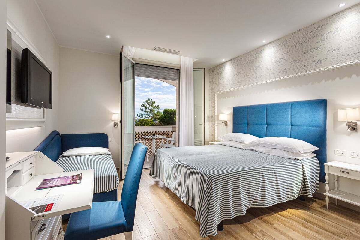 Quarto de hotel com cama, escrivaninha, cadeira e varanda com vista.