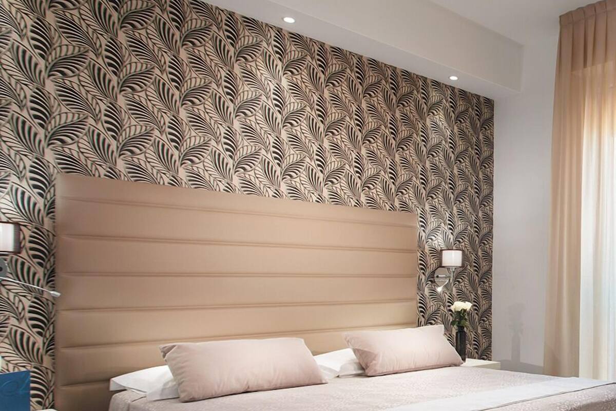 Quarto moderno com uma cama grande, papel de parede estampado e uma mesa de cabeceira com abajur.