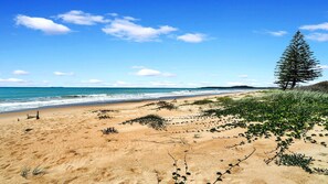 A beach with sand, sparse vegetation, and a clear sky. - Moomba On Main - Beachfront cottage in Wooli (WOOLI)